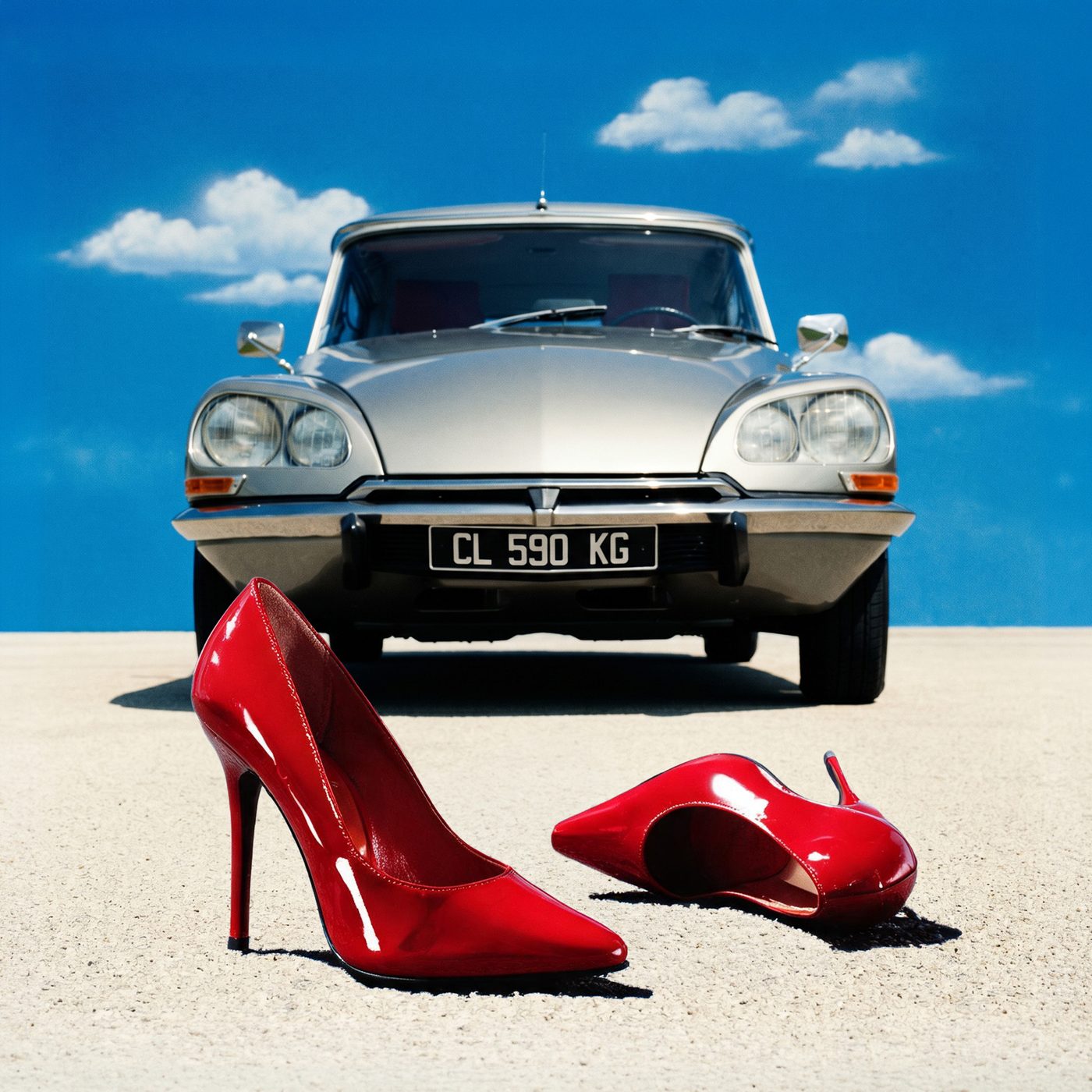 Un paio di décolleté rosse in primo piano davanti a una Citroën DS sotto un cielo blu